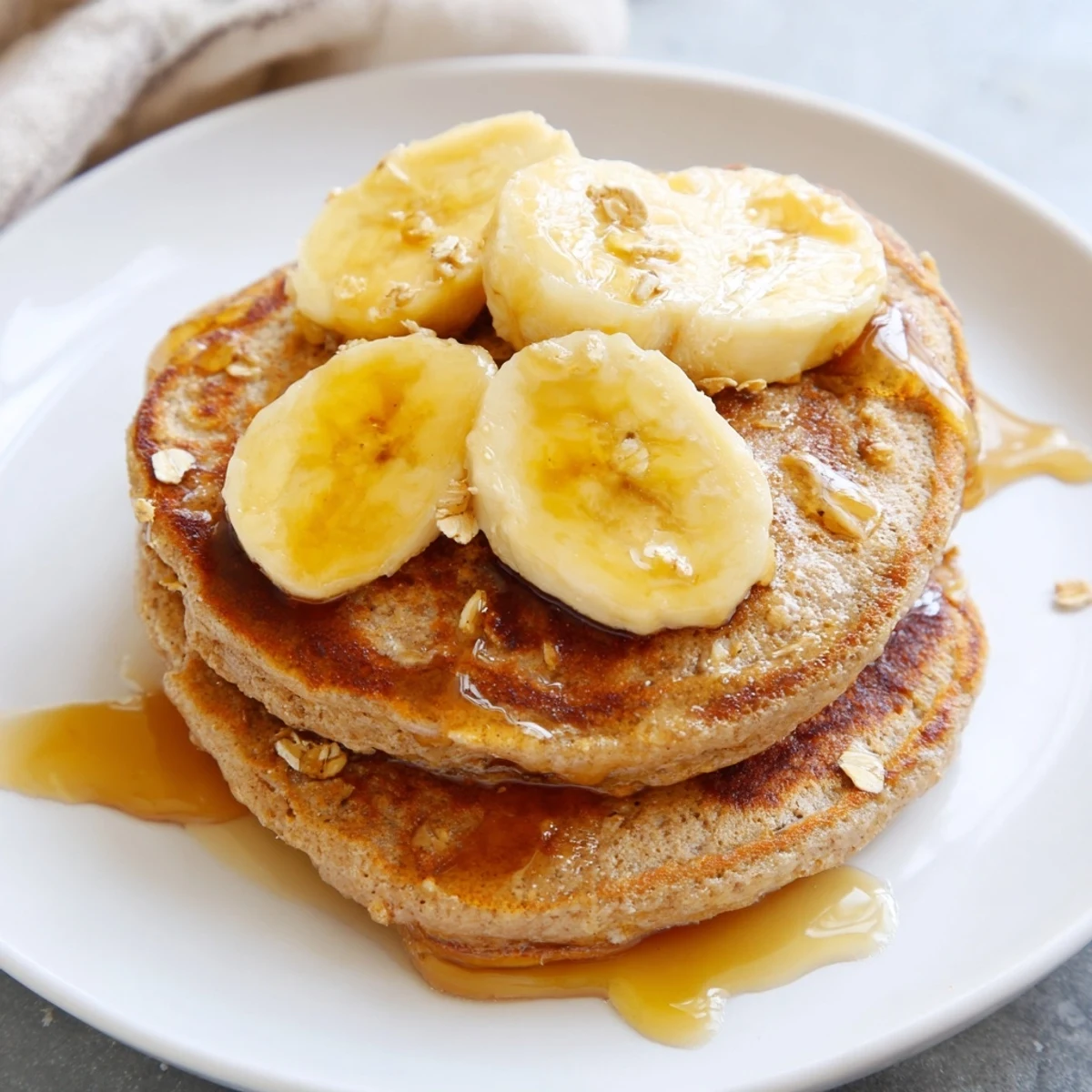 Golden-brown banana oat pancakes drizzled with maple syrup, a perfect easy breakfast.