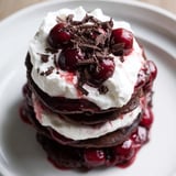 Stack of tempting Black Forest Pancake Minis featuring vibrant cherries and a dusting of dark chocolate shavings.