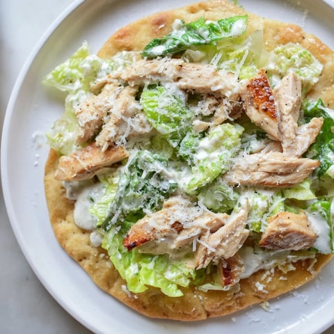 Goldene Caesar Chicken Flatbread mit knusprigem Salat und Parmesan, serviert mit Zitronenscheiben.