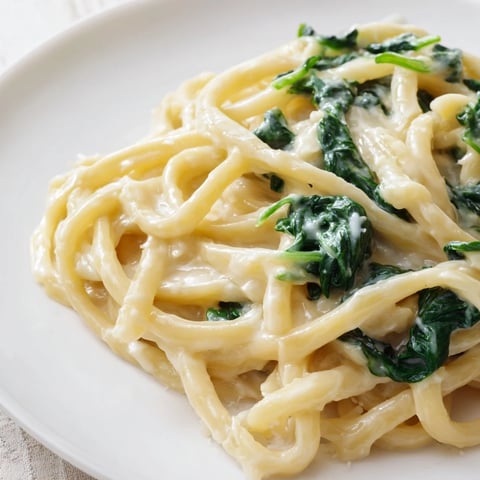 Cremige Spinat-Knoblauch-Nudeln serviert in einer tiefe Schüssel, belegt mit geriebenem Parmesan und einem Hauch roter Chiliflocken.