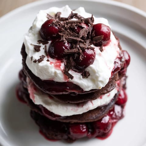 Stack of tempting Black Forest Pancake Minis featuring vibrant cherries and a dusting of dark chocolate shavings.