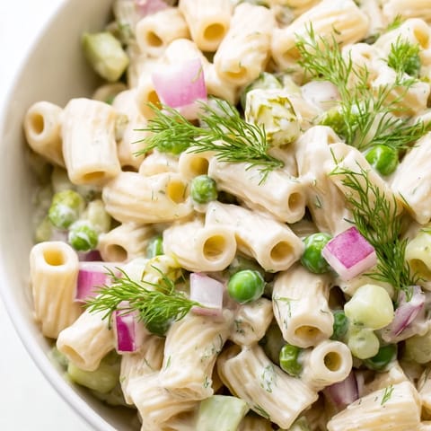 Ein Schüssel mit cremiger Dill-Pickle-Pasta-Salat mit ditalini, knackigen Gurken und erbsen in einer zitronig-sahnigen Sauce.