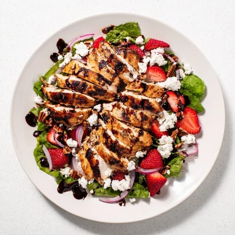 Frischer Strawberry Balsamic Chicken Salad auf einer Platte mit gegrillten Hähnchenbruststreifen, reifen Erdbeeren und Feta auf gemischtem Salat.