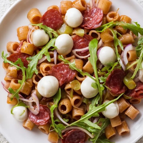 Eine bunte Frühlings-Antipasto-Pasta-Salat-Schüssel mit ditalini, peppigem Rucola, würzigem Salami und cremiger Mozzarella.  