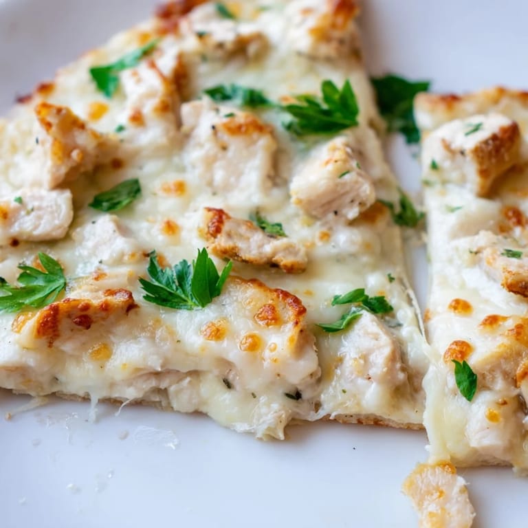 Frisch gebackene Chicken Alfredo Pizza mit glänzendem Käse, roten Zwiebelringen und Petersilie, serviert auf rustikalem Holzteller für den Küchentisch.