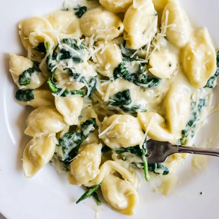 Ein Teller frisch gekochte Spinat-Knoblauch-Nudeln, von einer reichhaltigen cremigen Sauce umhüllt und garniert mit glasigem Zwiebelringen.